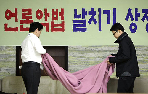 한나라당의 미디어법 상정이 이뤄진 국회 문방위 회의실 앞에서 밤을 지샌 당직자들이 26일 한나라당을 규탄하는 대형 플래카드 앞에서 침구를 정리하고 있다. 민주당은 한나라당의 미디어법 본회의 상정을 위한 표결을 막기위해 문방위 회의실에서 의원총회를 지속적으로 열 예정이다. 